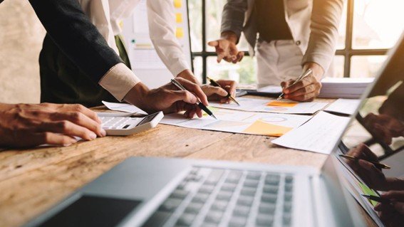 detalhe de mãos trabalhando, anaotando sobre mesa, papeis e notebook